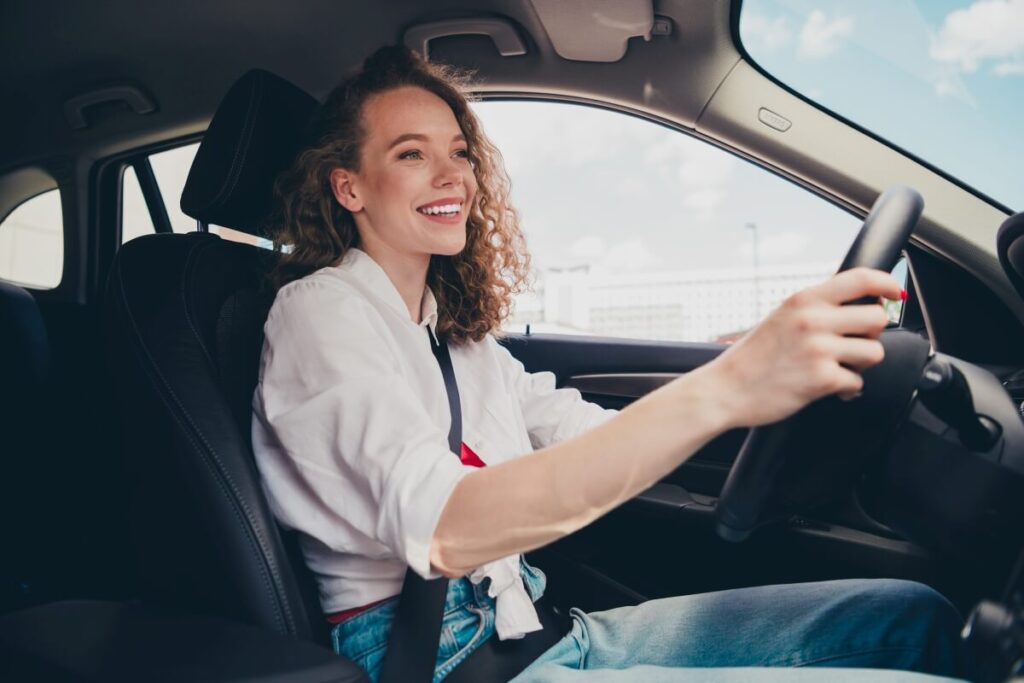 Młoda kobieta z uśmiechem prowadzi samochód podczas lekcji w szkole jazdy.