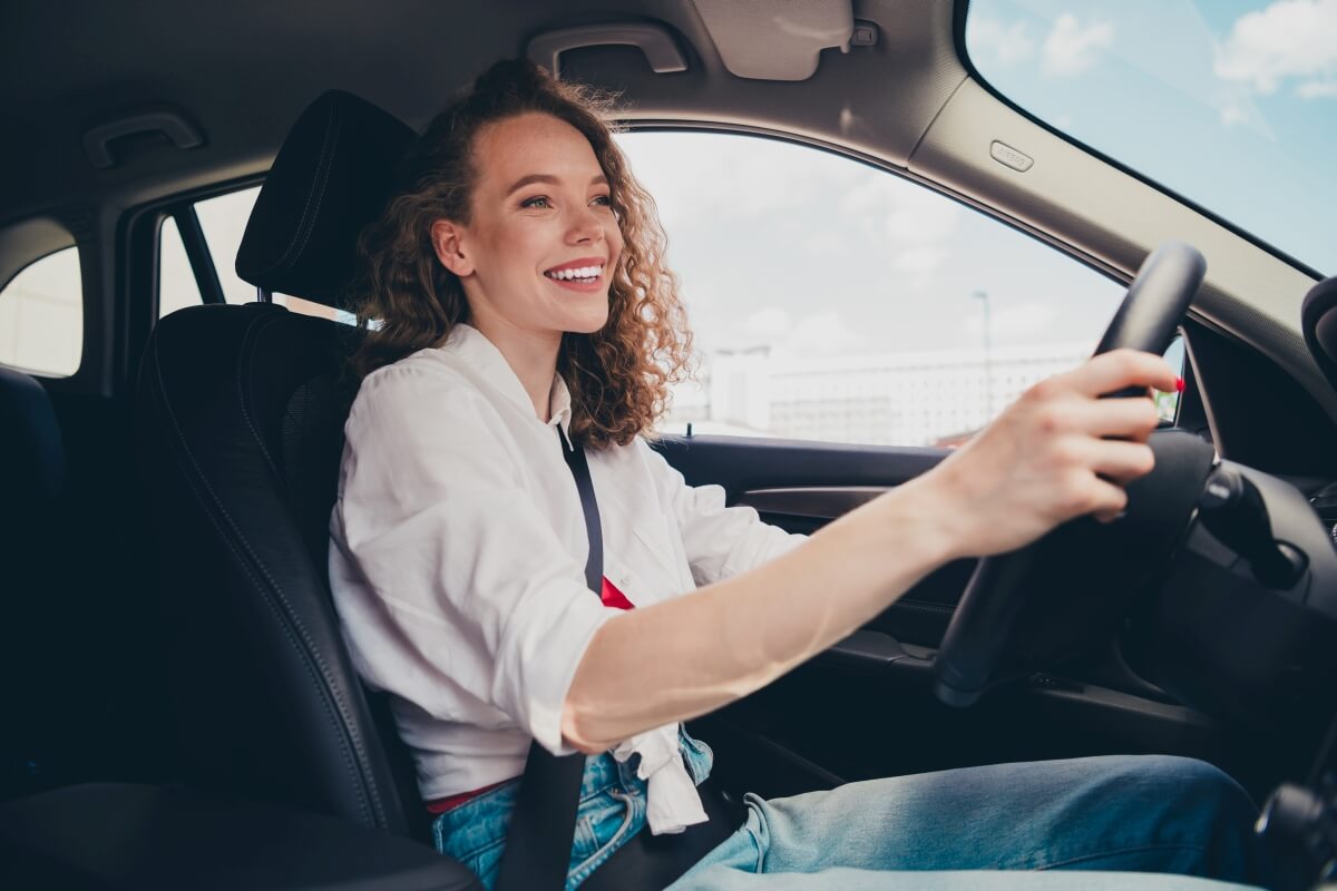Młoda kobieta z uśmiechem prowadzi samochód podczas lekcji w szkole jazdy.