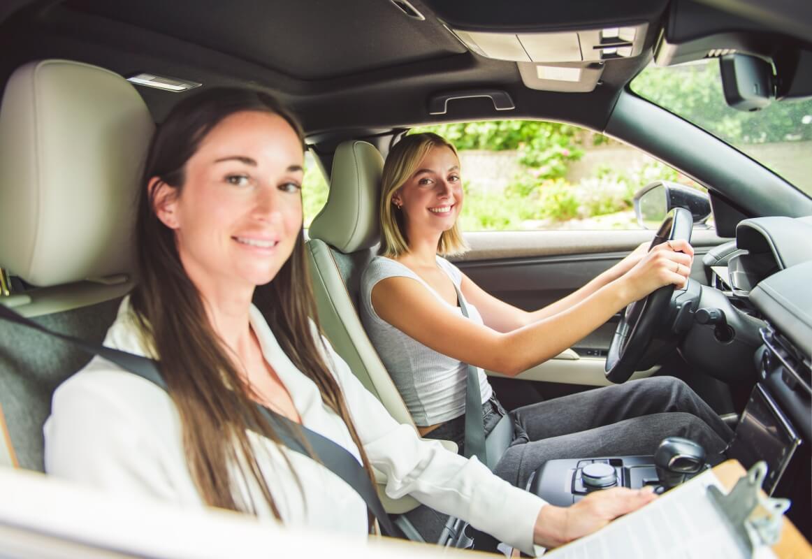 Młoda kobieta za kierownicą samochodu uczestniczy w jeździe doszkalającej z instruktorką.